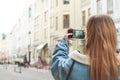 Girl travels in the old town and makes a photo landscape on a smartphone. Back view. Tourist in a jeans jacket photographs a city