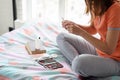 Girl treats nails with a nail file, sitting on a bed by the window of a bedroom Royalty Free Stock Photo