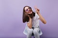 Girl in trendy white clothes posing with peace sign while listening music. Stunning woman in headph Royalty Free Stock Photo