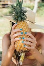 Girl with a turquoise manicure holds a ripe pineapple in her hands.