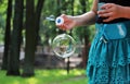 Girl in turquoise skirt let one large bubble in the summer park.