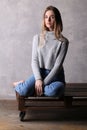 Girl in turtleneck sitting on a board. Gray background Royalty Free Stock Photo