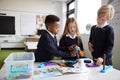 A girl and two boys standing at a table in a primary school classroom working together with toy construction blocks, close up