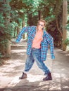 A girl with two pigtails in a plaid shirt with oversleeves and oversized jeans stands in a pose on a green alley. Dance Royalty Free Stock Photo