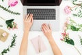 Girl typing on laptop. Office workspace with female hands, laptop, notebook and pink flowers on white background. Top view. Flat