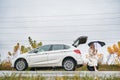 Girl with umbrella sitting on spare tire near open car. Royalty Free Stock Photo