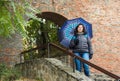 A girl with an umbrella stands on a rainy day on a staircase near the aisle in the city wall in Sibiu city in Romania