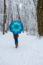 Girl under blue umbrella in snowy forest. Snowfall concept. Woman under wet snow rain in winter park.