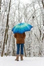 Girl under blue umbrella in snowy forest unfocused. Snowfall concept. Woman under wet snow rain in winter park. Royalty Free Stock Photo