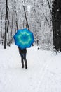 Girl under blue umbrella in snowy forest unfocused. Snowfall concept. Woman under wet snow rain in winter park. Royalty Free Stock Photo