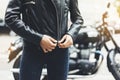 Girl unfastens black leather jacket on background motorcycle in sun flare atmospheric city, hipster biker female hands closeup Royalty Free Stock Photo