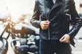 Girl unfastens black leather jacket on background motorcycle in sun flare atmospheric city, hipster biker female hands closeup Royalty Free Stock Photo