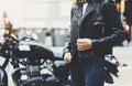 Girl unfastens black leather jacket on background motorcycle in sun flare atmospheric city, hipster biker female hands closeup Royalty Free Stock Photo