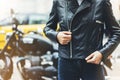 Girl unfastens black leather jacket on background motorcycle taxi in sun flare atmospheric city, hipster biker female hands Royalty Free Stock Photo