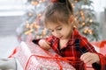 Girl unties a red bow on a Christmas gift while sitting on a bed