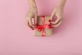 Girl unties a ribbon bow on a gift box with hands, female with present wrapped in decorative paper on pink background, top view,