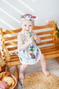 A girl up to a year old in a kitchen apron and a bow on her head sits on a bench, next to tartlets with booths