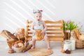 A girl up to a year old in a kitchen apron and a bow on her head sits on a bench, next to tartlets with booths