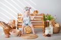 A girl up to a year old in a kitchen apron and a bow on her head sits on a bench, next to tartlets with booths