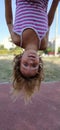 Girl upside down. A child with blond hair in a striped pink dress hangs from a bar in the playground. The hair hangs down Royalty Free Stock Photo