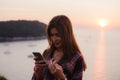 Girl using cellphone near the sea in sunrise or sunset. Royalty Free Stock Photo