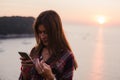 Girl using cellphone near the sea in sunrise or sunset. Royalty Free Stock Photo