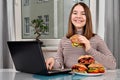 Girl using a laptop and eating a vegetarian sandwich at home Royalty Free Stock Photo