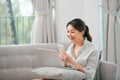 Girl using laptop and smartphone. Young woman in casual clothes with her legs crossed sitting on sofa at cozy home interior. Royalty Free Stock Photo