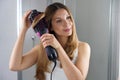 Girl using round brush hair dryer to style hair at the mirror in an easy way at home Royalty Free Stock Photo