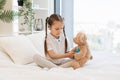 Girl using stethoscope to check toy bear on bed Royalty Free Stock Photo