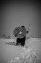 A girl in a Valkyrie costume climbs a snowy mountain and holds a sword and shield in her hands. Royalty Free Stock Photo