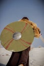 A girl in a Valkyrie costume climbs a snowy mountain and holds a sword and shield in her hands. Royalty Free Stock Photo