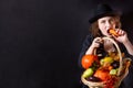 A girl in a vampire costume with yellow eyes holds a basket with vegetables. Bright emotion. Conceptual photo