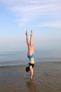 girl with long legs with her head down and feet in the air doing gymnastics on the seashore in summer Royalty Free Stock Photo