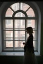 girl in vintage clothes stands alone at the window of an old building, silhouette in profile