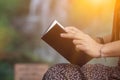 Girl in vintage dress sits holding Bible to read and study God`s teachings alone on blurred background of nature. Concept of Royalty Free Stock Photo