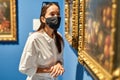 visitor wearing an antivirus mask standing near pictures in museum of arts