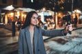 Girl vlogger recording with digital camera. Smiling woman taking selfie video on light night city. Traveler making video