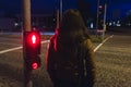 Girl waiting to cross a street in night red light is shining