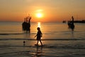 The girl walked on the beach with a fishing boat and sunset.