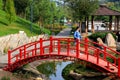 The girl is walking along Old red wooden bridge across mall river in Japanese park. Vintage style Japanese bridge above water. Royalty Free Stock Photo