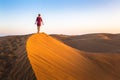 Girl walking on sand dunes in arid desert at sunset and wearing dress, scenic landscape of Sahara or Middle East Royalty Free Stock Photo