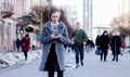Girl walking and texting on the smart phone in the street wearing a gray coat, in the winter