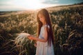 Girl walking on a wheat field holding wheat spike at beautiful sunset. Freedom and fresh air concept. Royalty Free Stock Photo