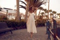 A girl walks along the beach in the evening, palm trees. Girl in a long white boho dress in a tropical city.