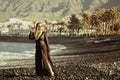 A girl walks along a stone beach in a long black pareo. Summer day, a woman rests against the background of palm trees. A girl in Royalty Free Stock Photo