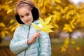 A Girl Walks In An Autumn Park With Yellow Leaves, In Warm Headphones And A Blue Insulated Jacket