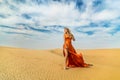 Girl walks on desert. Beautiful woman is walking, staing on sand or dune, touches, shows her legs. Blonde lady in