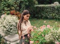 A girl walks in a flowering garden, she has a vintage blouse with a bow, chestnut long hair. she gently cares for her Royalty Free Stock Photo