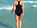 Girl walks into the sea in a black swimsuit back view Royalty Free Stock Photo